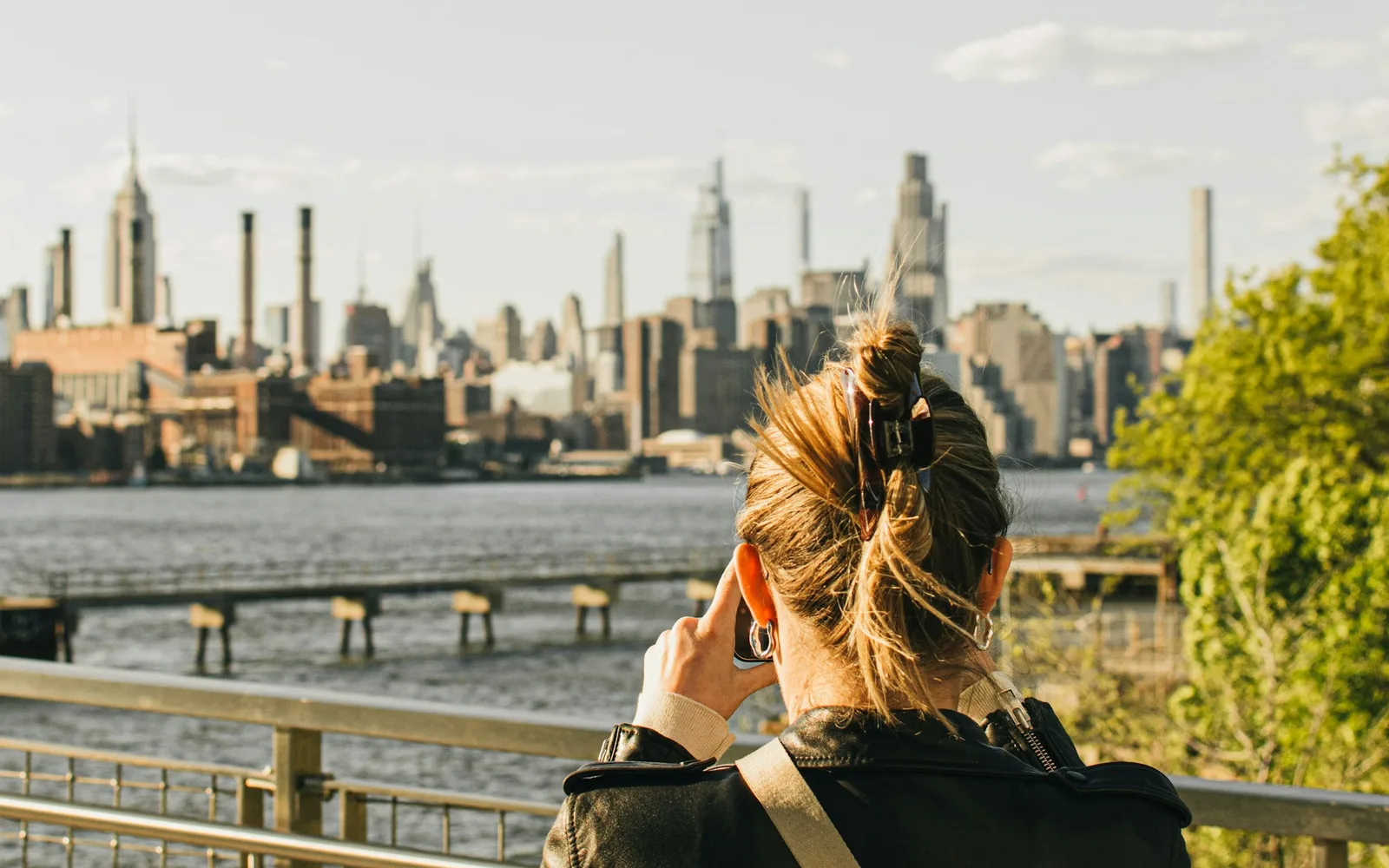 Traveler holding a phone up to photograph the Manhattan skyline across the river