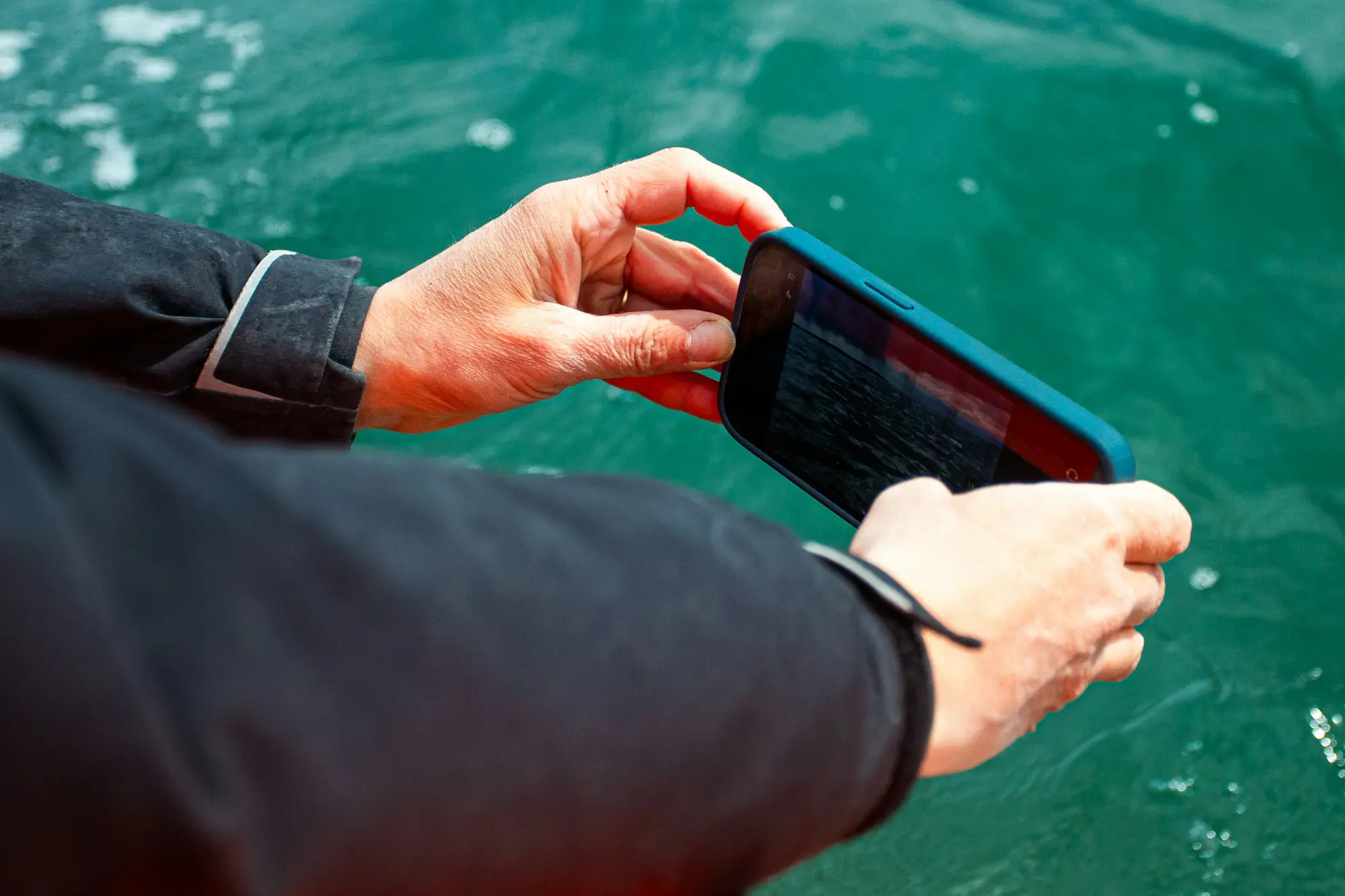 Hands holding a smartphone near turquoise water on a travel activity